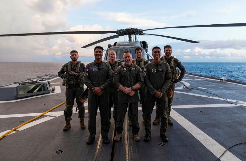 Several men in uniform stand on the flight deck of a ship in front of a helicopter.