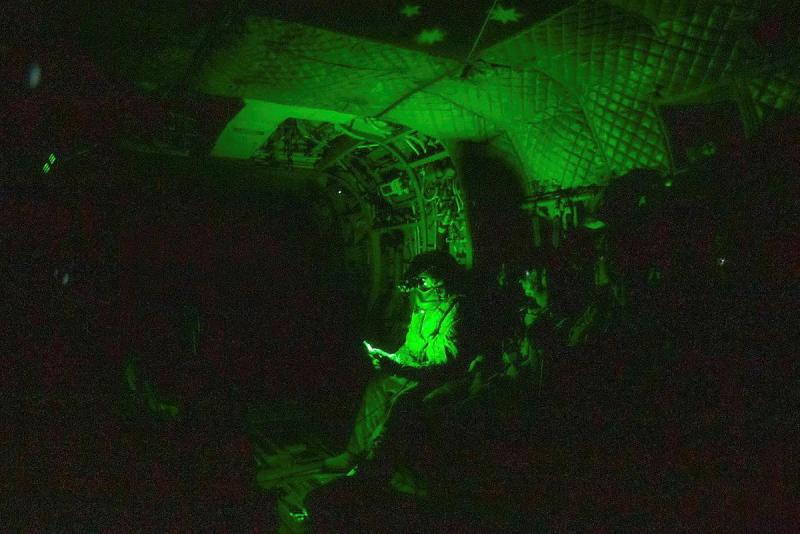 A soldier sits in green light inside an Army helicopter.