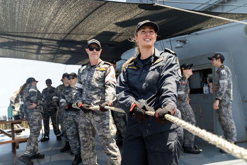 Several people in uniform stand one behind another in a line holding a rope.