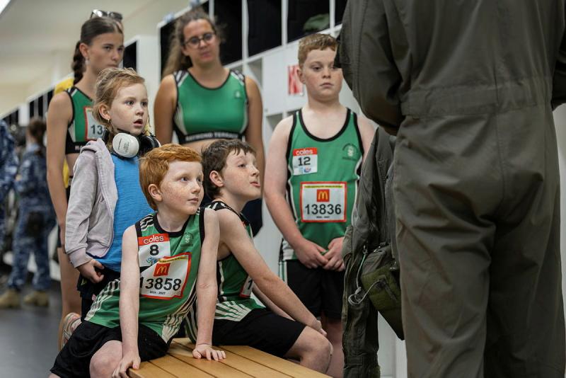 A group of youth athletes look up to a person in a flight suit while in a locker room.