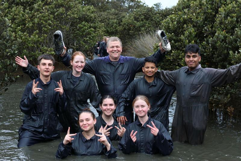 A group of people standing chest to waist high in water in a mangrove.