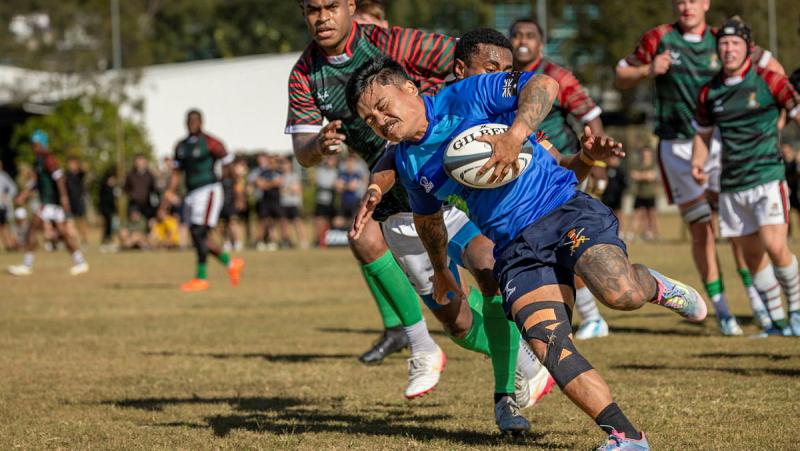 A man runs with a rugby ball while other players chase him across a field.