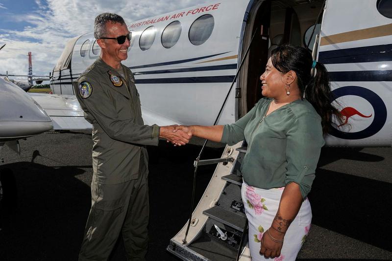Man in uniform shakes the hand of a woman as both stand beside a plane