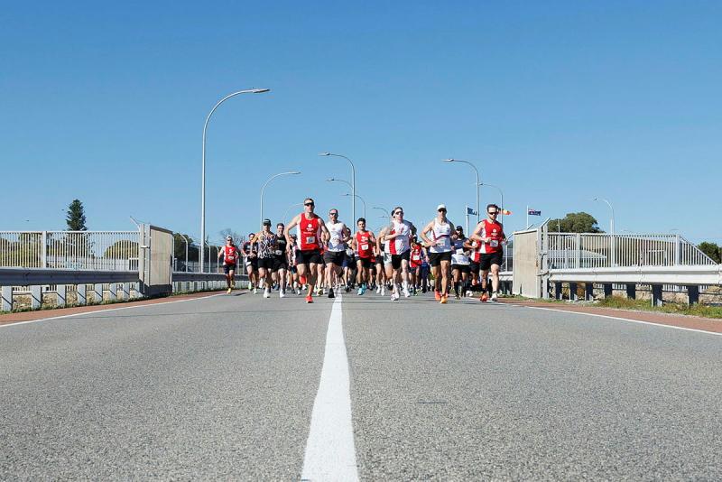 A large group of people run down a road.