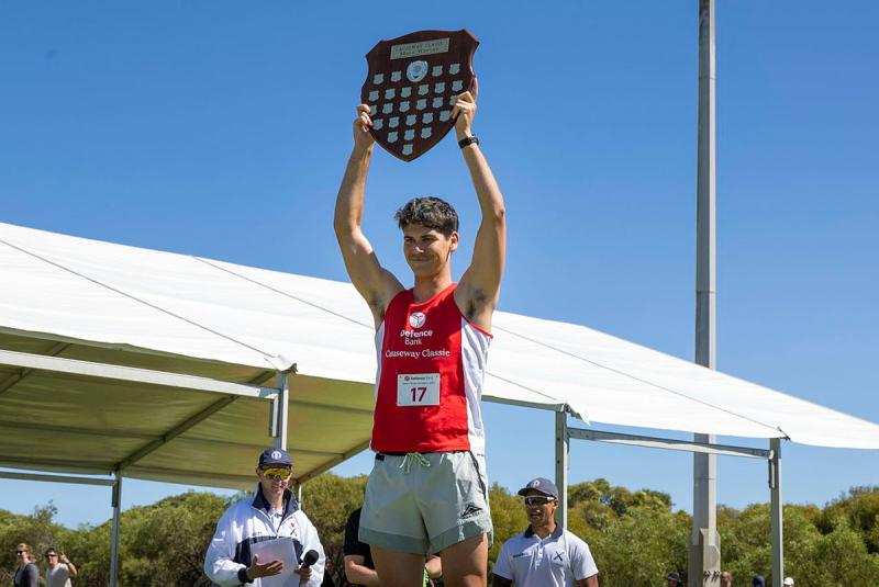 A male runner holds a trophy crest above his head.