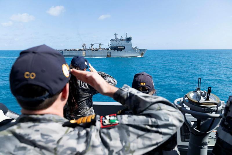 People on one ship salute towards a ship in the distance.