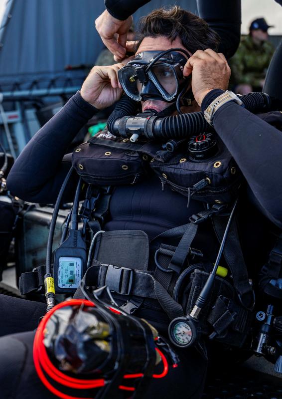 A man in diving gear puts on his goggles and breathing tube.