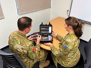 Two military personnel side at a desk looking through a medical kit.