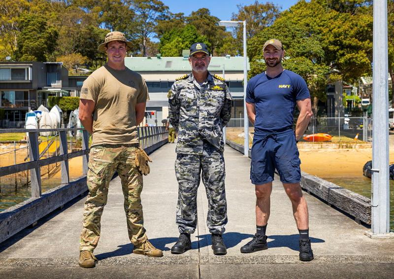 Three military me stand with their arms behind their backs on a pier.