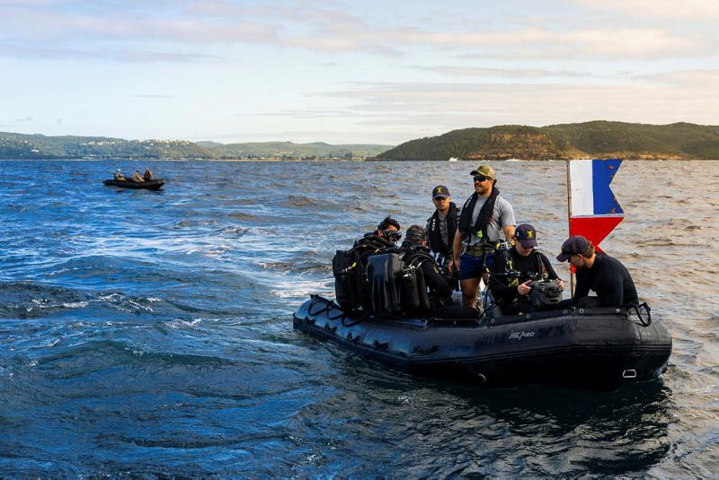 A group of people travel through the water in a small boat, some in diving gear, with another small boat behind them.
