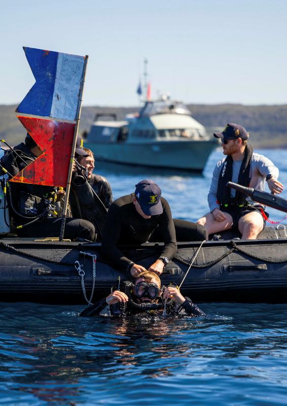 A person in diving gear is in the water next to a small boat, with other people in the boat.