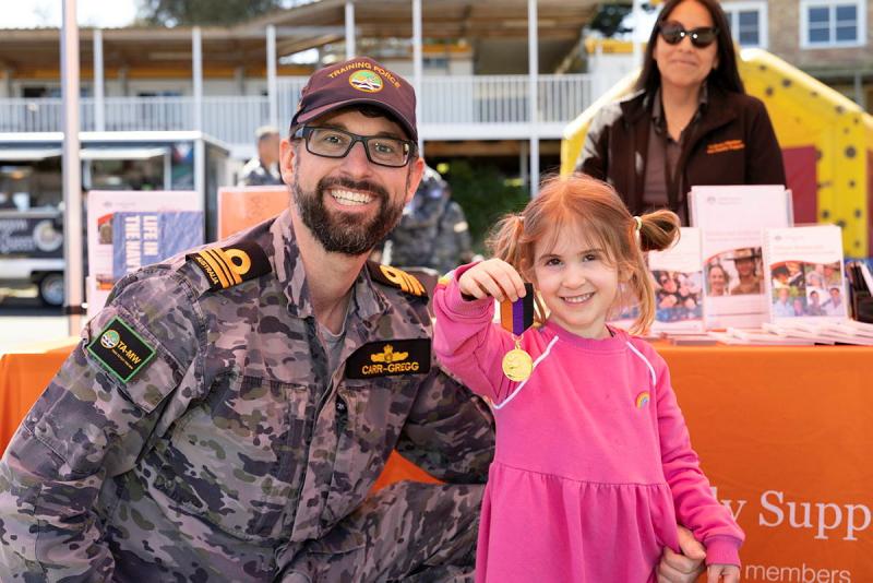 A father smiles with his daughter as she shows off a medal.