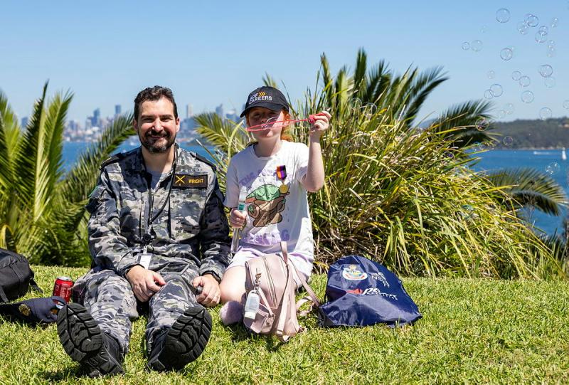 A man sits with his daughter as she blows bubbles.