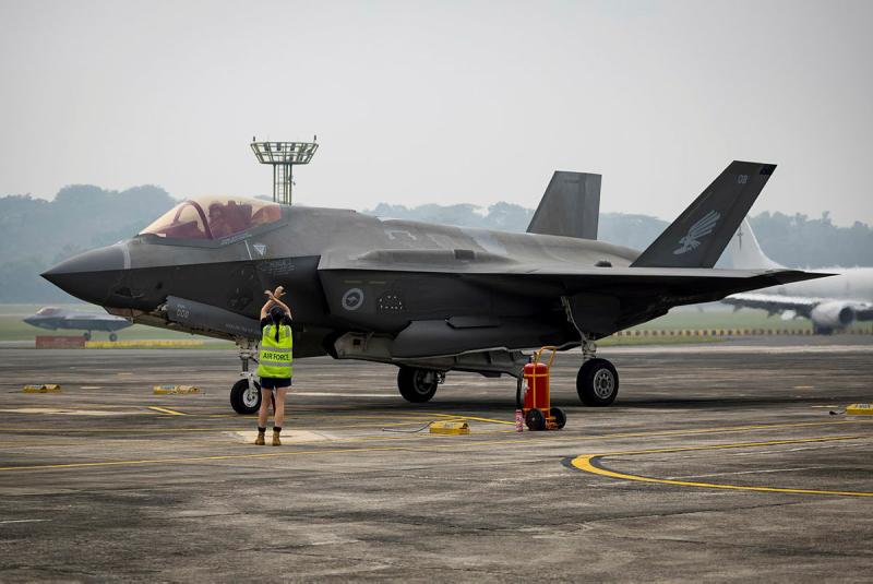An Air Force member crosses her arms in the air as a signal to the pilot in an aircraft nearby.