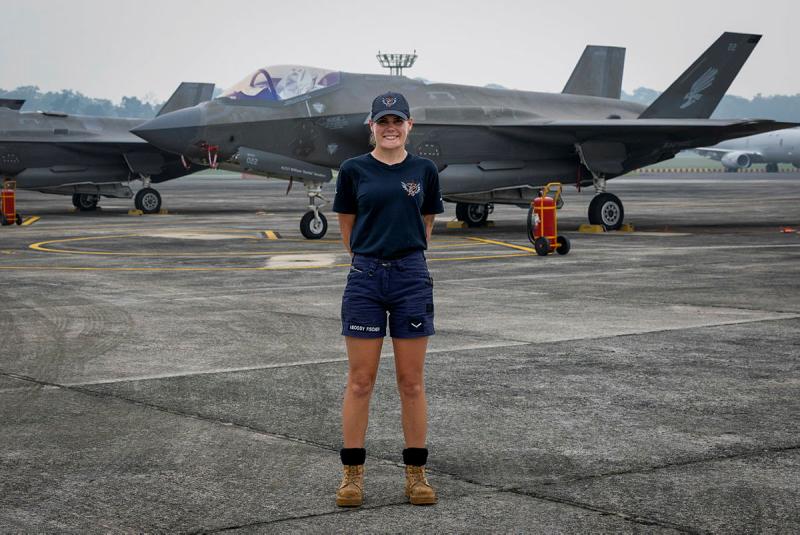 A military woman stands before several aircraft on the tarmac.