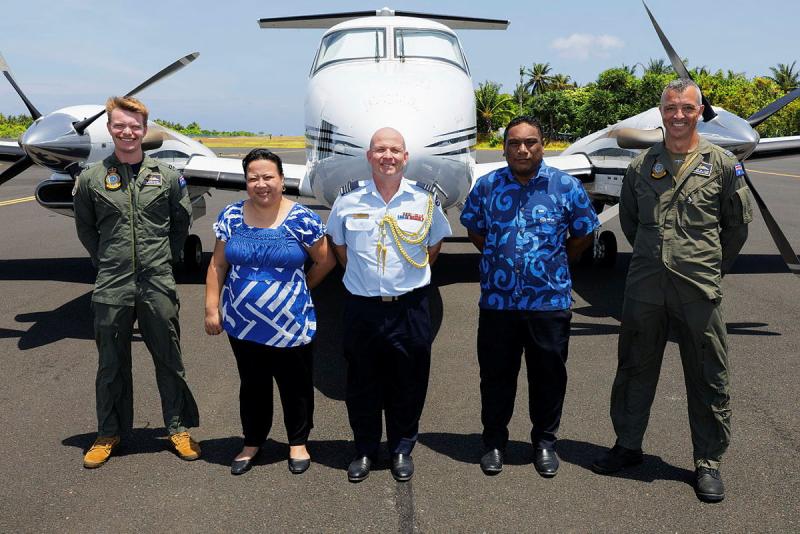 Three military men and two civilians stand in front of an aircraft.