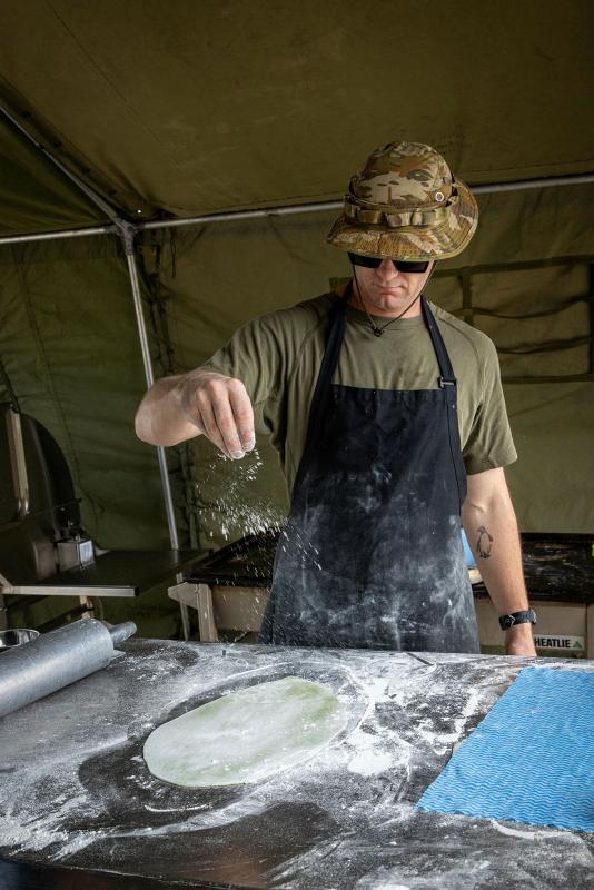 A man sprinkles flour on dough rolled out on a flour-covered table.