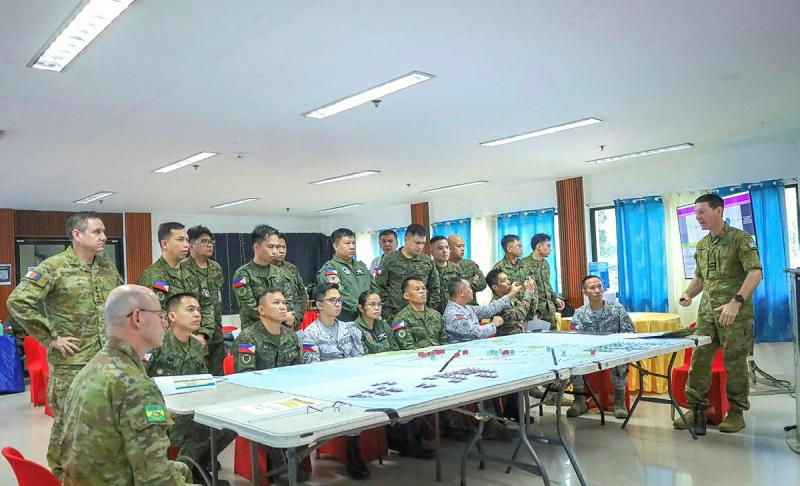 People in uniform sit and stand around a large table covered with a planning map and markers.