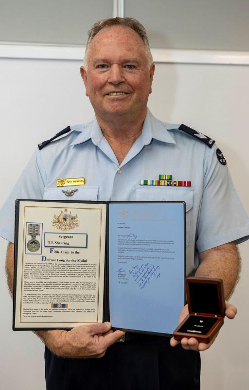 A man in Air Force uniform stands holding a certificate and a open giftbox containing a small metal object.