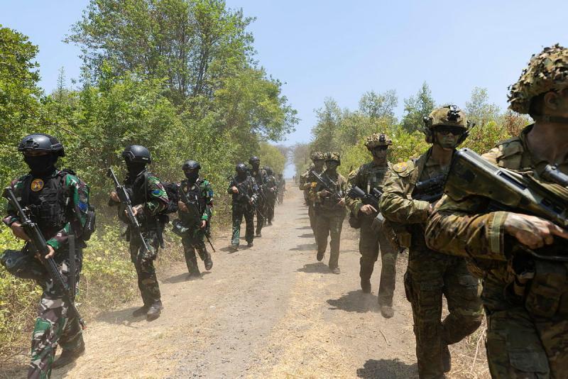 Two lines of armed soldiers march down a dirt path.
