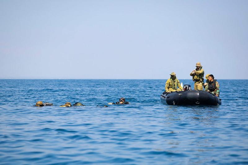Military divers in the ocean water with soldiers standing in an inflatable raft.