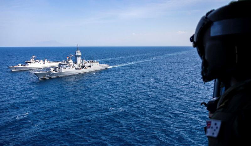 Two ships sail next to each other in the ocean while a person looks out of a helicopter.
