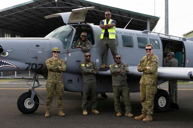 Six military men stand on, in and around an aircraft.