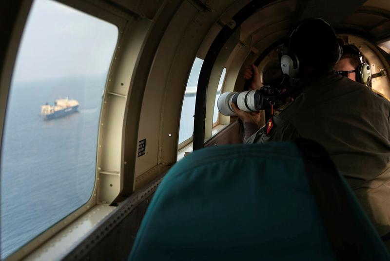 Two men in an aircraft take a photo of a ship out at sea.