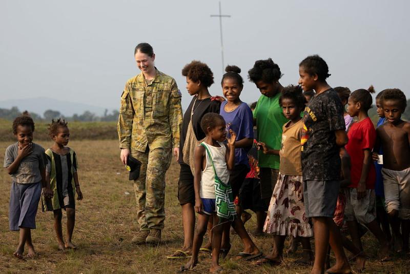 A military woman walks with a group of children.