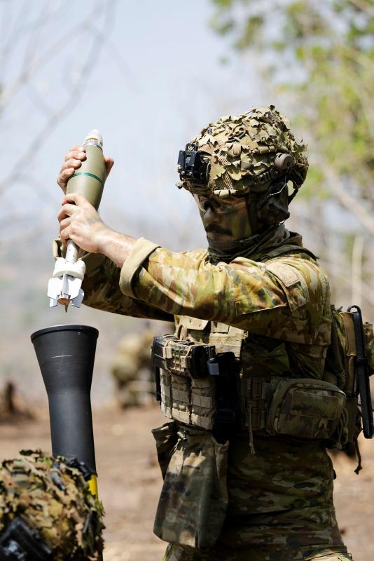 A man in uniform holds a mortar round above a mortar tube before loading it.