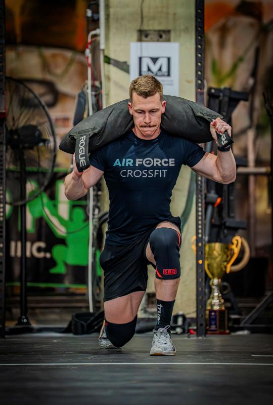 A man from Air Force CrossFit does a lunge with a weighted sack on his shoulders.