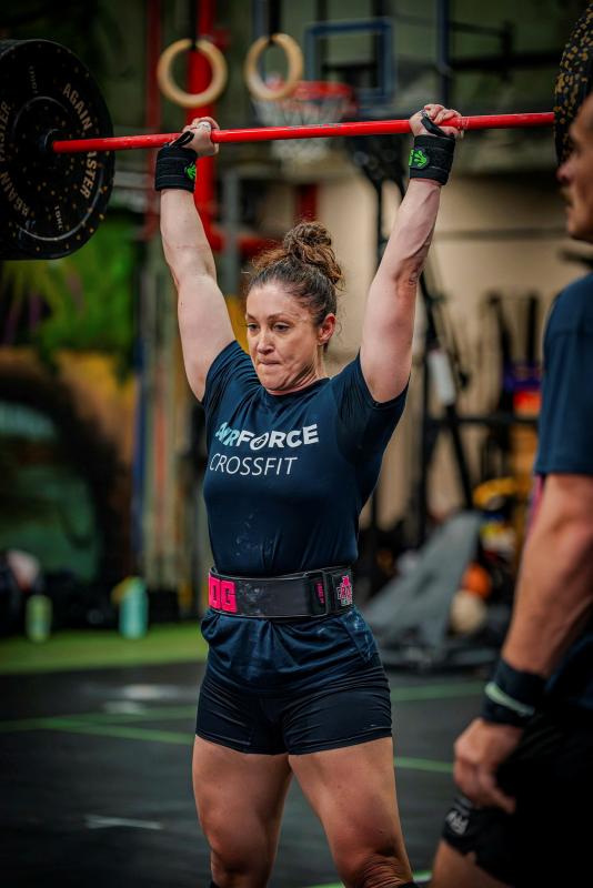 A woman from Air Force CrossFit does a shoulder press with a weighted bar.