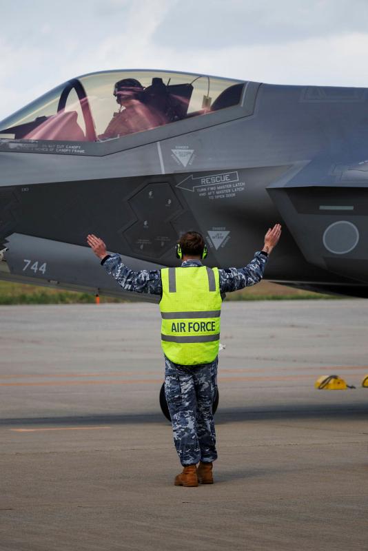 An Air Force member signals with both arms in the air to a pilot in an aircraft.