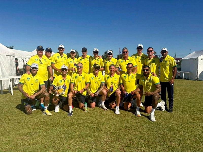 A group of men in matching yellow and green uniform stand or kneel together on grass.