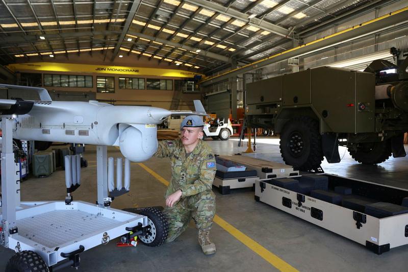 A man in uniform crouches to look at a small aircraft in a warehouse.