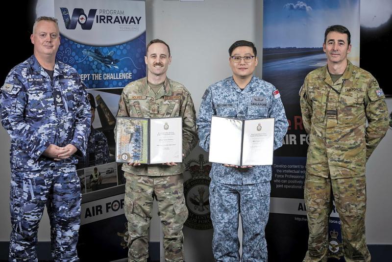 Two military men hold open certificate books and two military men stand on either side of them.