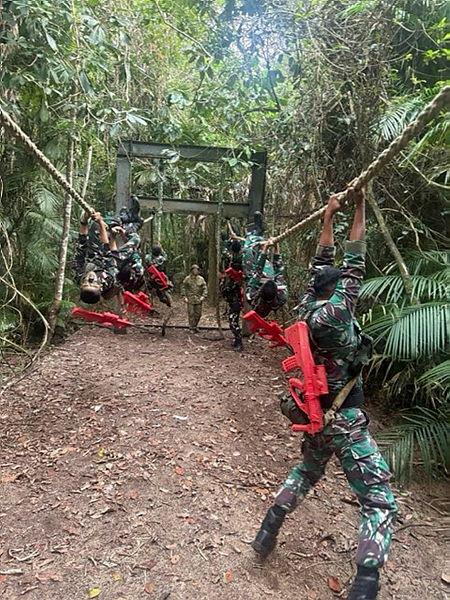 People in Indonesian Army uniform, with red replica guns slung over their shoulders, move along ropes as a person in Australian Army uniform stands between the ropes.