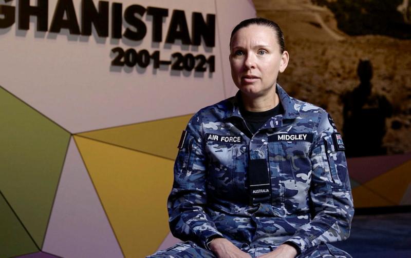 Woman sits in front of a wall with geometric designs and the words Afghanistan 2001 to 2021 on it