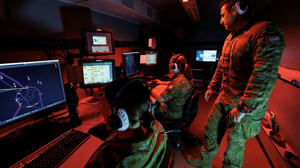 People sitting in a dark room in front of computer screens.