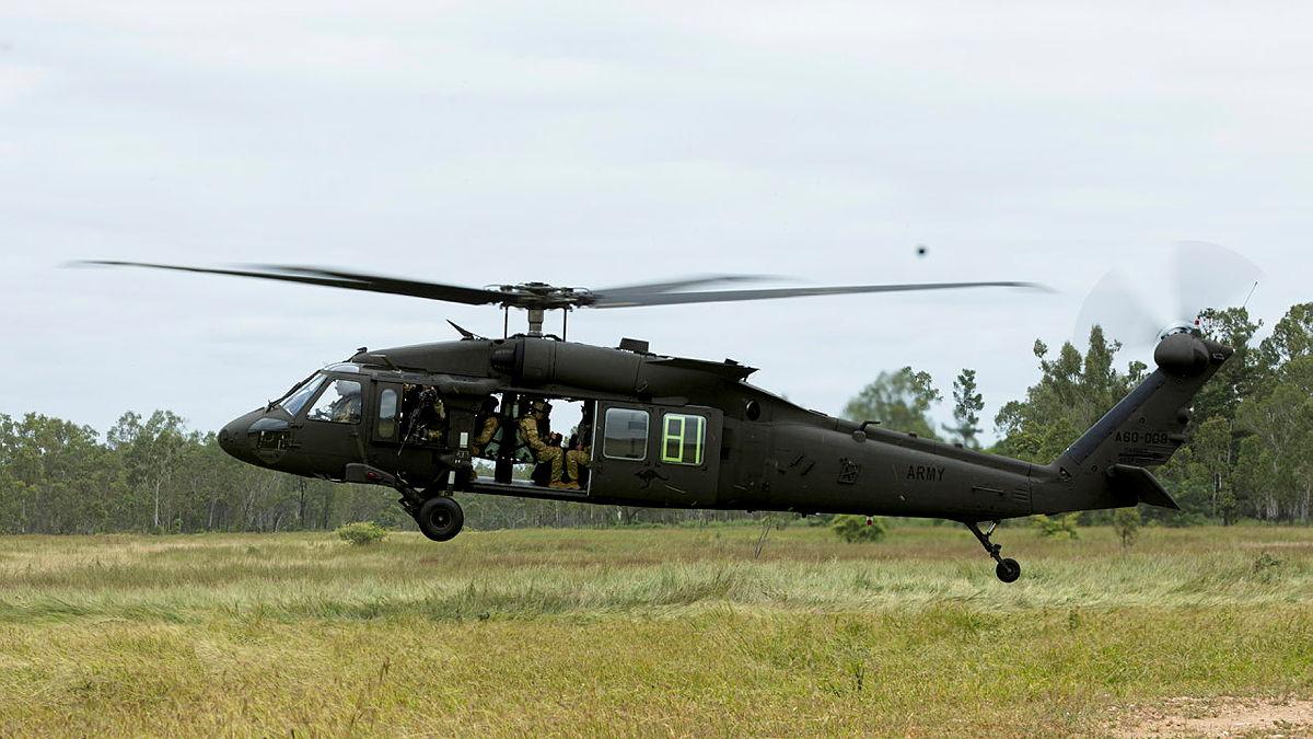 A black helicopter hovers above the ground.