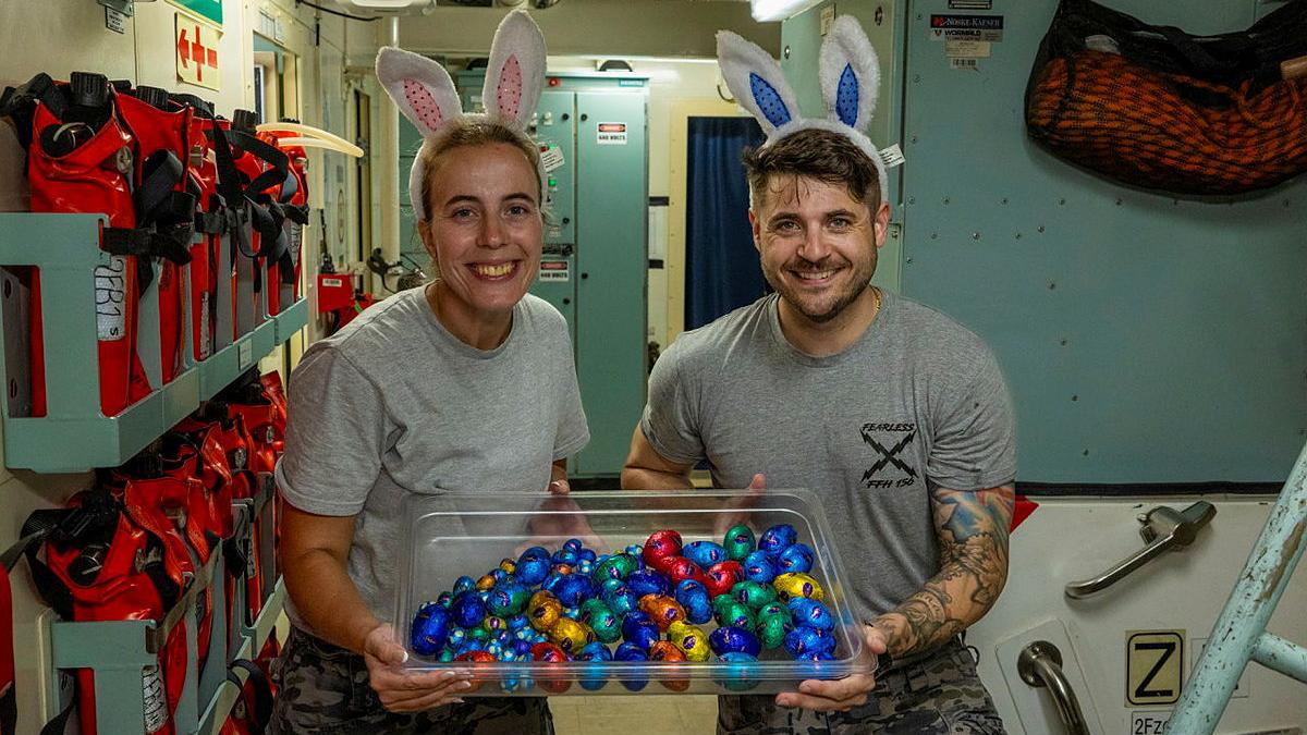 Two people wearing bunny ears hold a container full of Easter eggs.