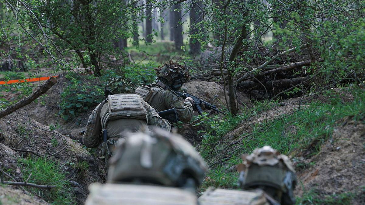 Military personnel crawl through trenches.