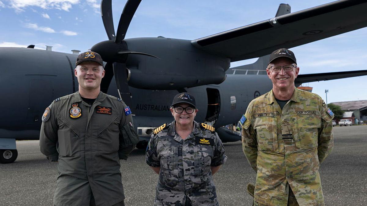 Three military personnel standing on front of a large aircraft on the tarmac.