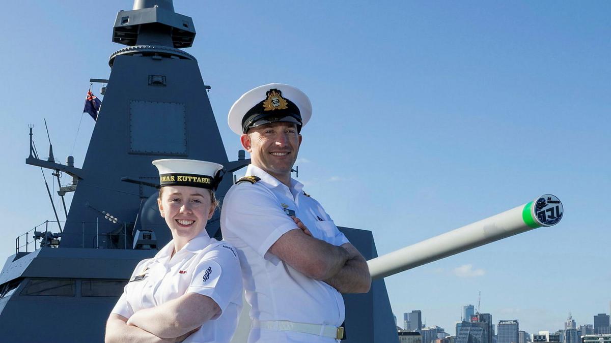Two Navy sailors stand back to back with their arms crossed while on a ship.