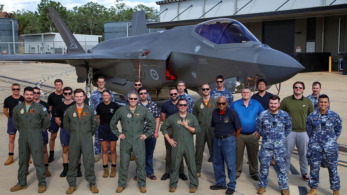 Military personnel stand before a stationary aircraft.