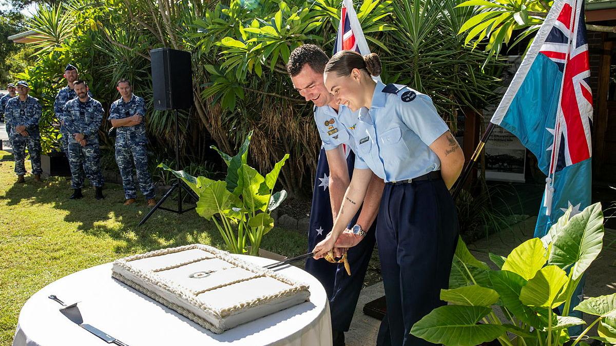 A man and a women in Air Force uniform cut a cake while outdoors in a garden.