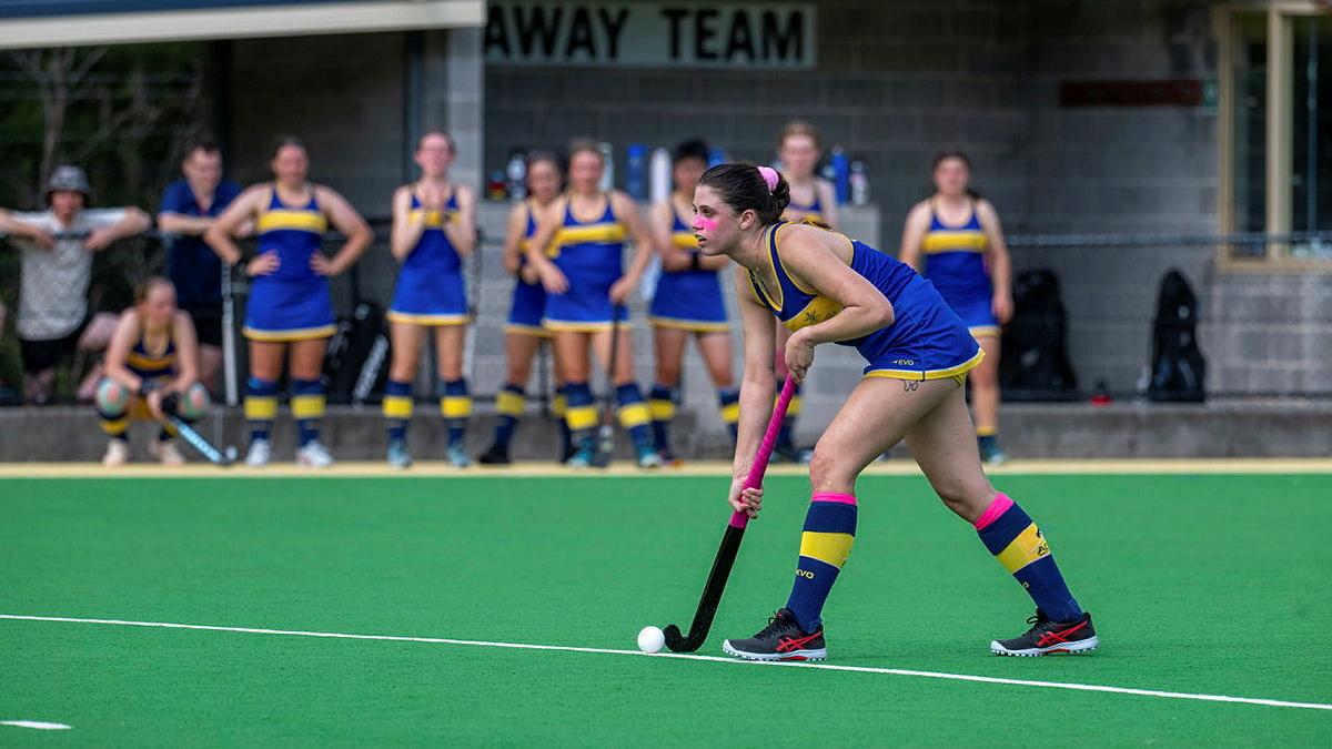 A woman on the hockey field in uniform ready to hit the ball.