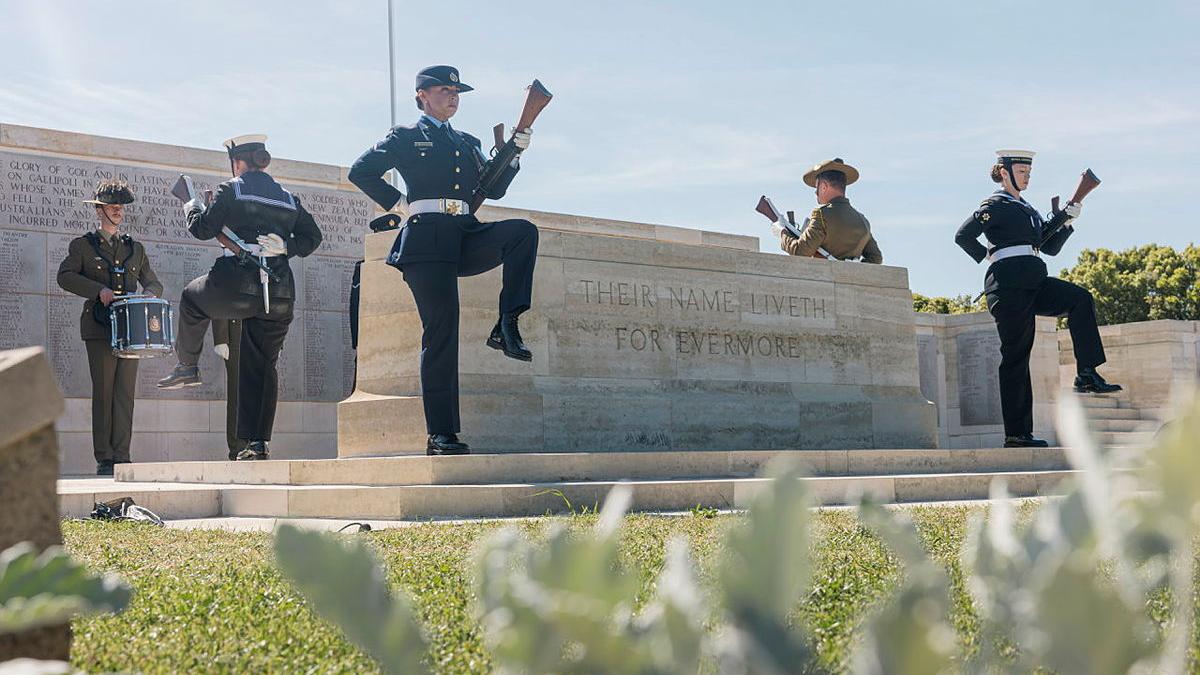 Four Australian Defence Force Federation Guard members march around a memorial stone with an Army drummer in the background.