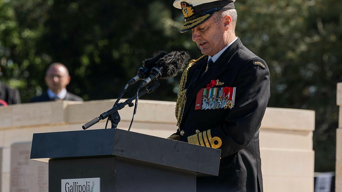 A man in formal Navy uniform speaks at a podium.