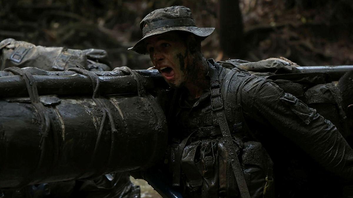A soldier in the jungle helping to carry a large litter on his shoulder.